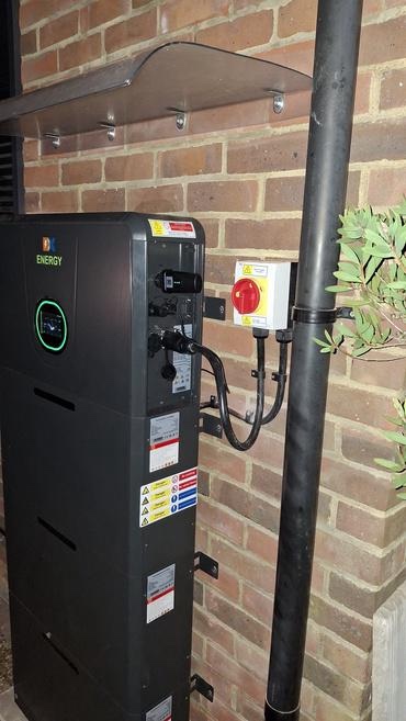 Weather canopy above the DX Energy battery unit, with the labelled AC isolator mounted alongside on the brick wall
